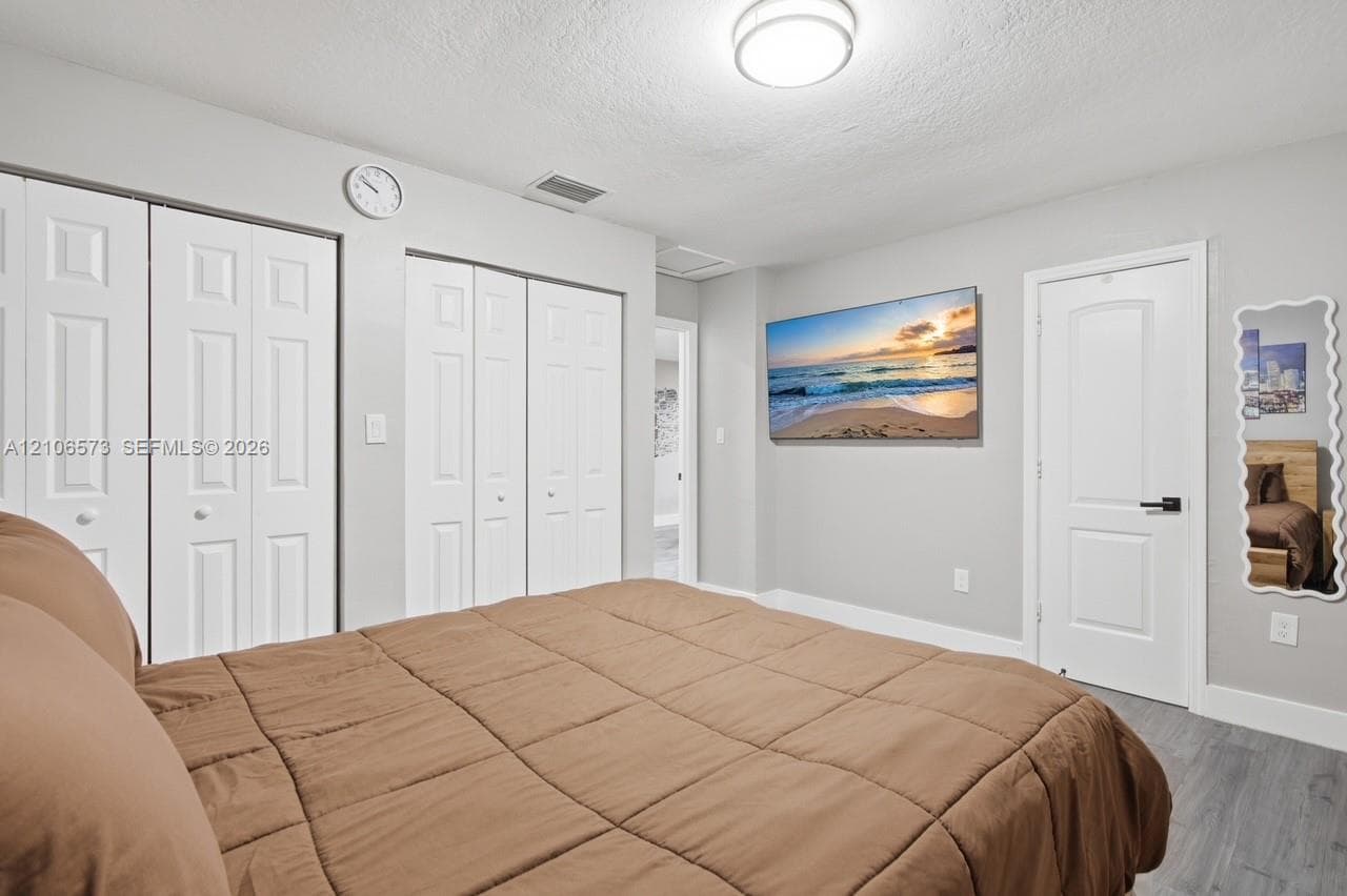 Room featuring wood-finish flooring, two sets of bifold closet doors, a solid-core interior door with matte black hardware, and a flush-mount ceiling light fixture