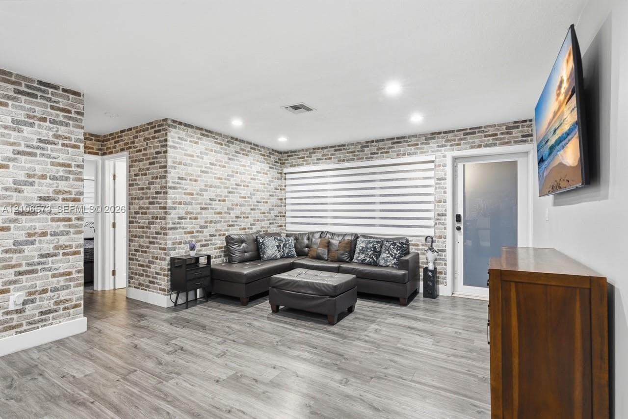 Interior featuring brick veneer accent walls, wood-finish flooring, recessed lighting, and a frosted glass exterior door