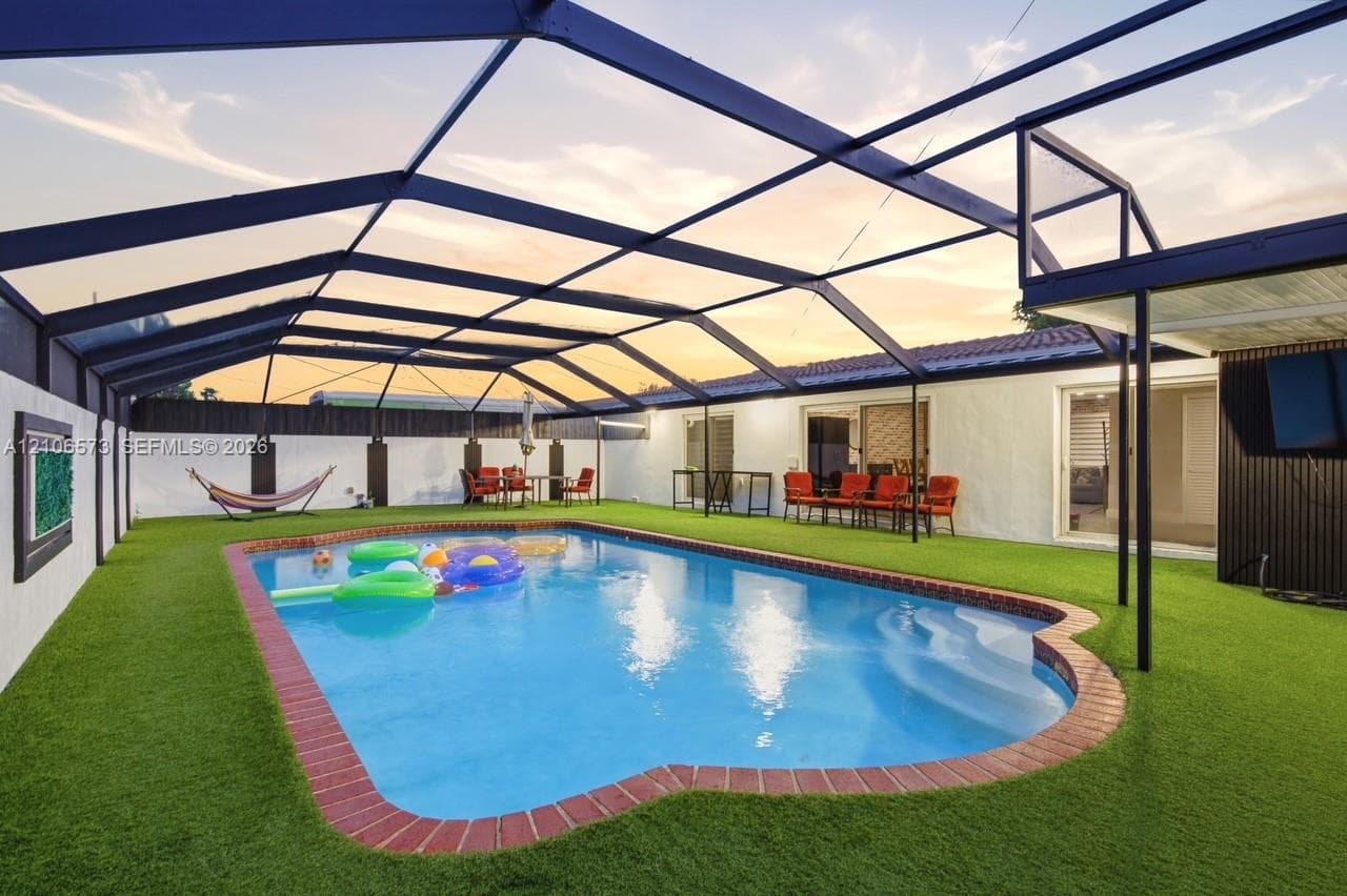 In-ground pool with brick coping, enclosed by a full-coverage metal screen lanai over artificial turf surfacing
