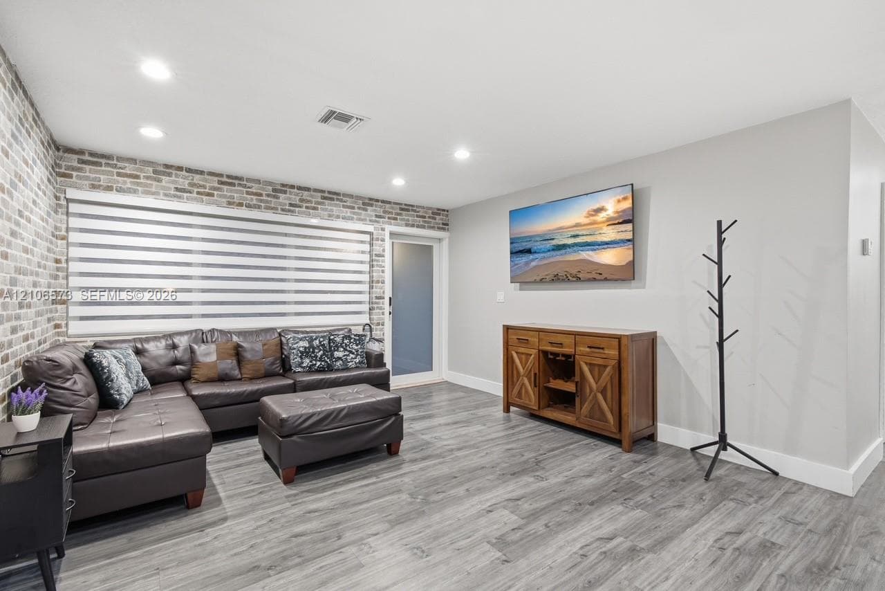 Interior space featuring a brick accent wall, wood-finish flooring, recessed lighting, and a frosted glass-panel door