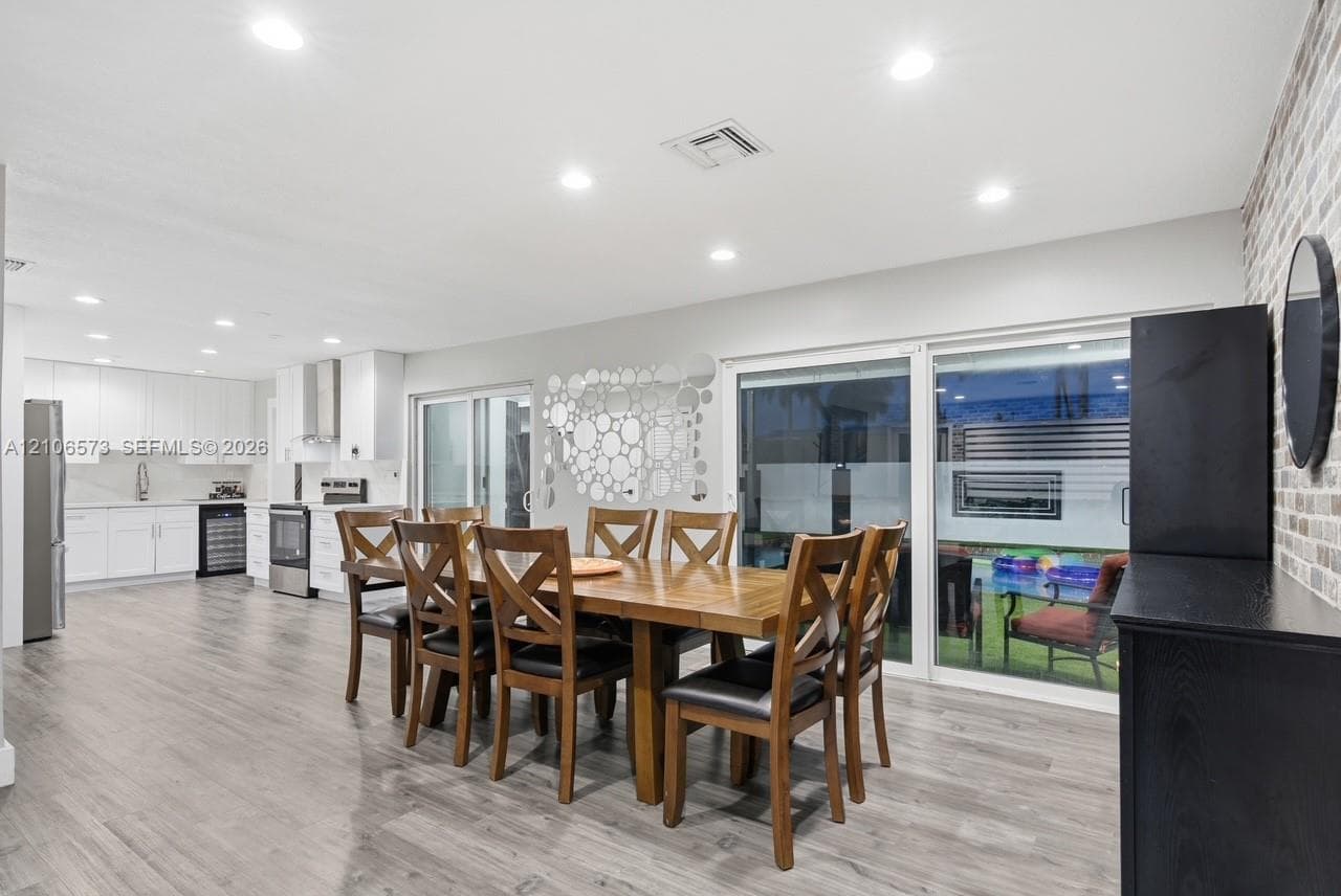 Open-concept interior featuring wood-finish flooring, recessed lighting, exposed brick wall detailing, white cabinetry, and dual sliding glass doors