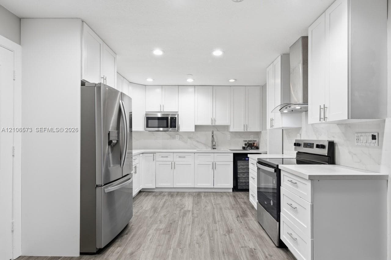 Kitchen featuring white shaker-style cabinetry, stainless steel appliances, stone-look backsplash, wood-finish flooring, and recessed ceiling lighting