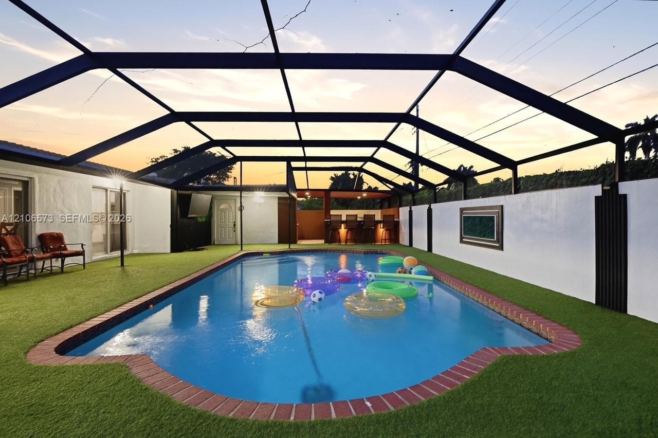 Screened-in pool area featuring brick coping, synthetic turf surfacing, and a built-in outdoor wet bar
