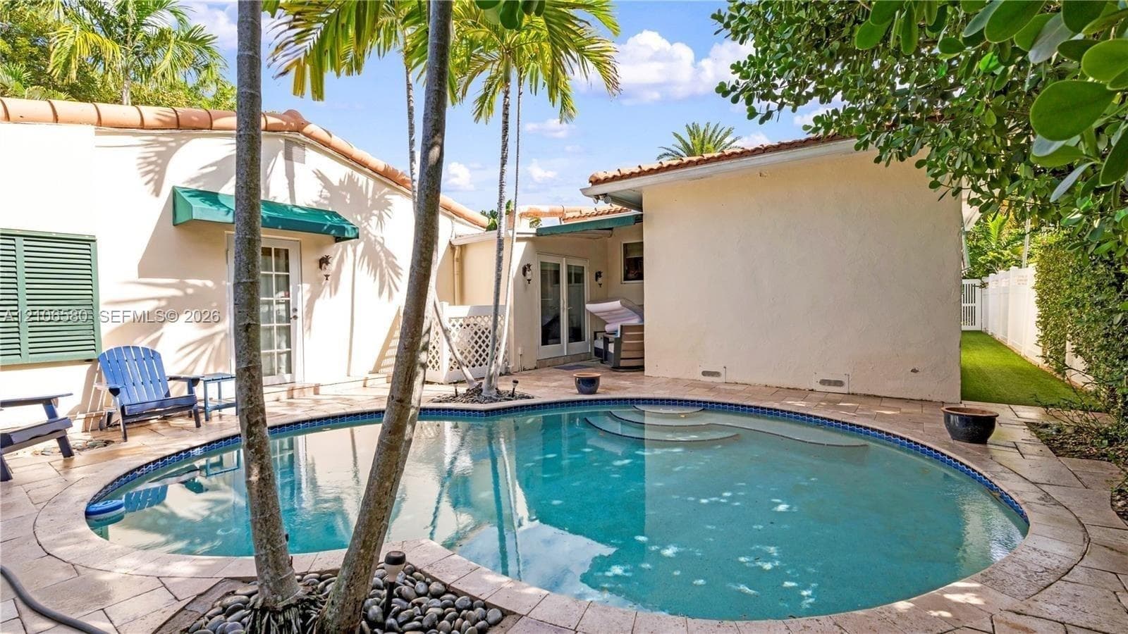 Exterior courtyard featuring a curved swimming pool, natural stone pool deck, built-in steps, and palm trees