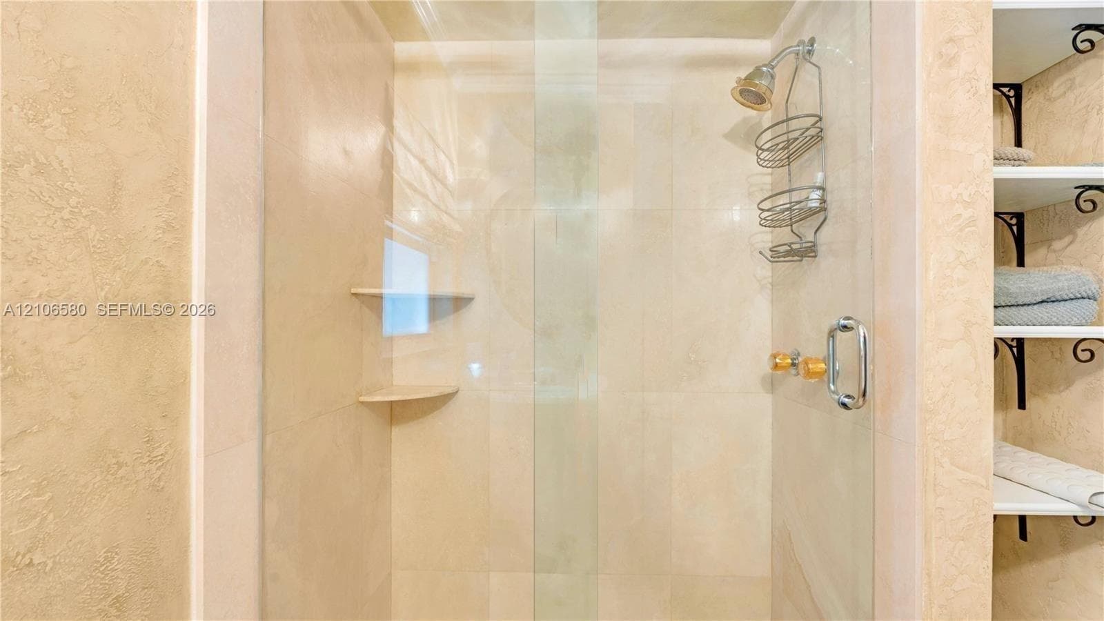 Walk-in shower featuring floor-to-ceiling stone-style tile, clear glass enclosure, built-in shelving, and metallic hardware
