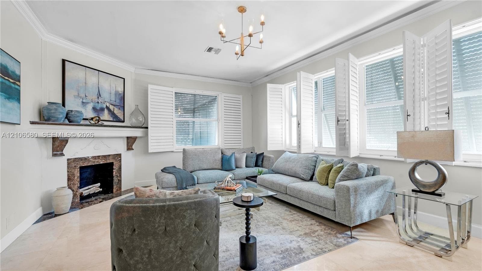 Living room featuring stone fireplace surround with mantel, multi-pane windows with white plantation shutters, crown molding, and polished stone flooring