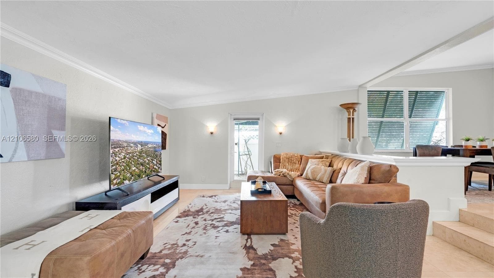 Living area featuring wall-mounted sconce lighting, crown molding, a half-wall partition, and multi-level floor elevation