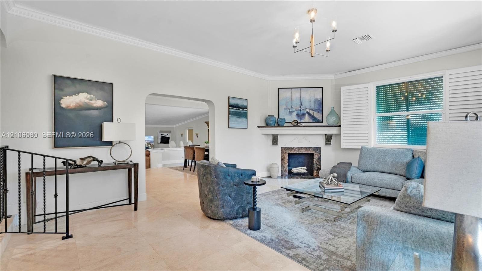 Living area featuring stone-finish flooring, a fireplace with a decorative mantel, crown molding, multi-light chandelier, and plantation shutters
