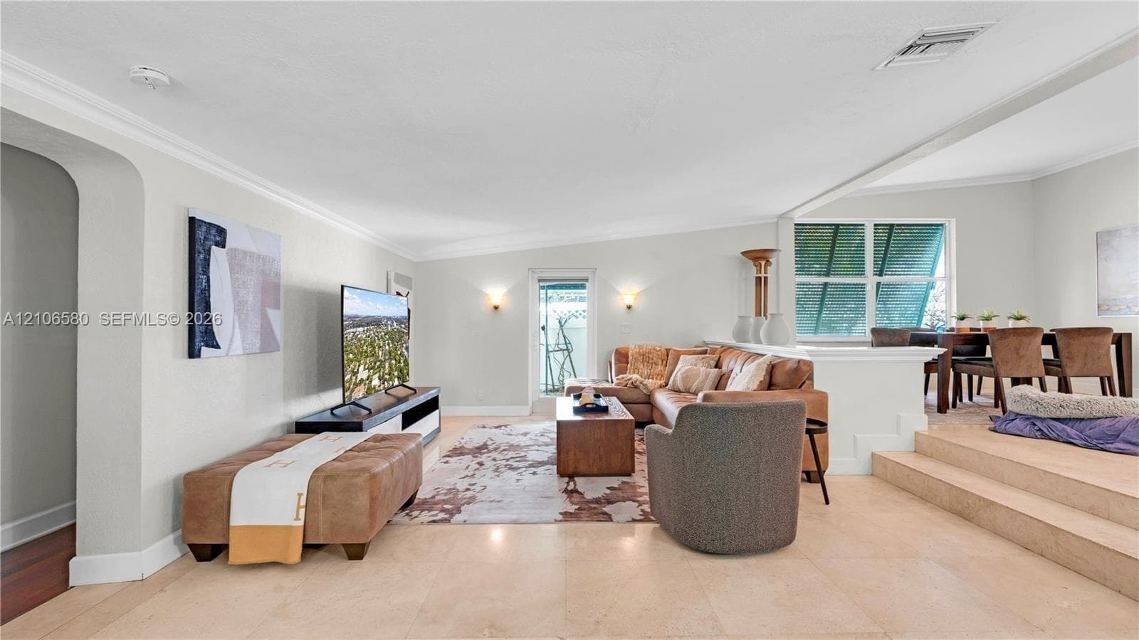 Open-concept floor plan featuring light-toned tile flooring, recessed crown molding, arched entryways, and a multi-level layout with a carpeted elevated platform