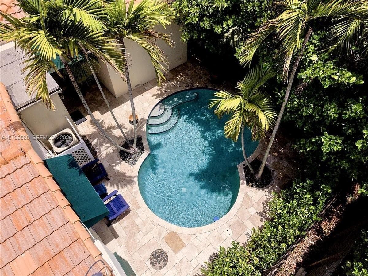 Curved swimming pool with built-in stairs, surrounded by stone-tile patio decking, mature palm trees, and perimeter landscaping