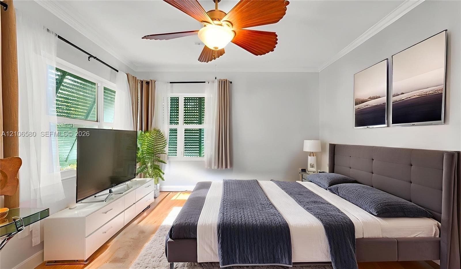 Wood-finish flooring, multi-blade ceiling fan with integrated lighting, crown molding, and windows featuring plantation-style shutters