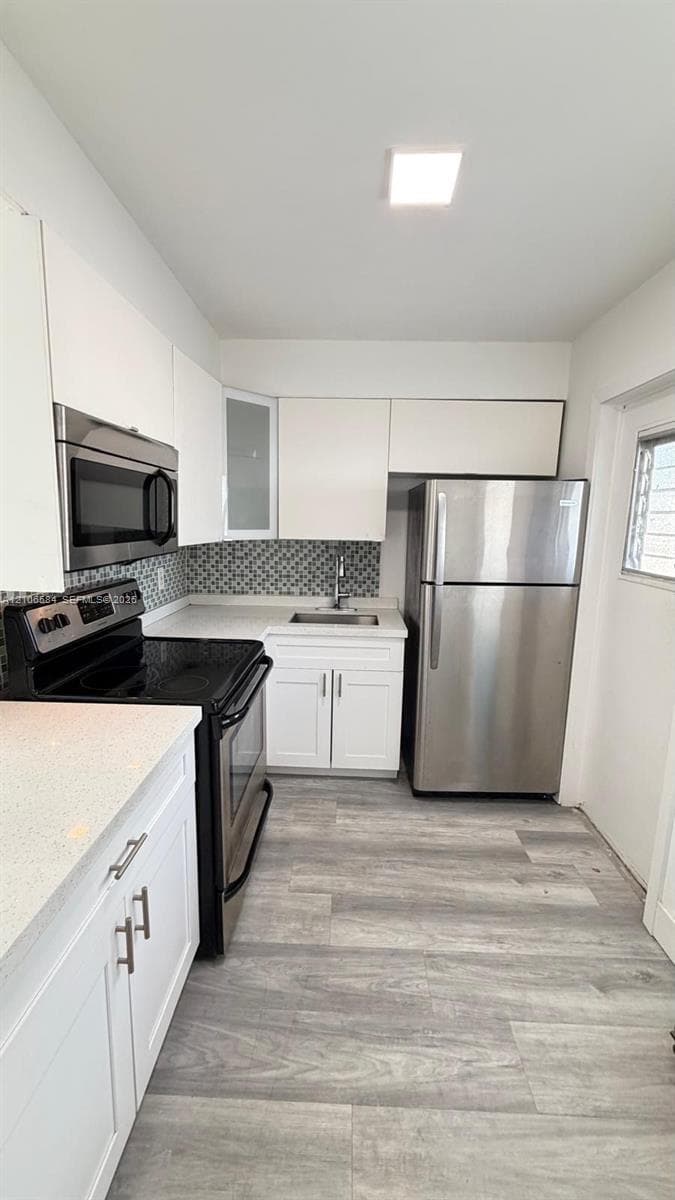 Kitchen featuring white cabinetry, wood-finish flooring, stone-style countertops, stainless steel appliances, and a geometric-patterned tile backsplash