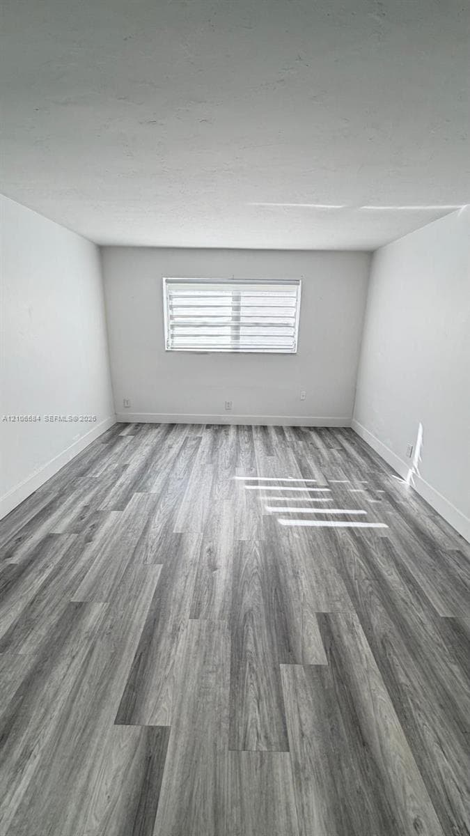 Neutral-toned interior space featuring wood-finish flooring and a single horizontal window with fitted blinds