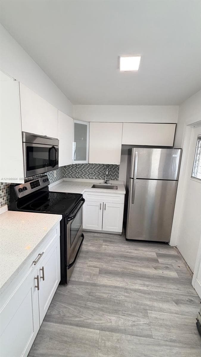 Kitchen featuring white cabinetry, stainless steel appliances, quartz countertops, mosaic tile backsplash, and wood-finish flooring