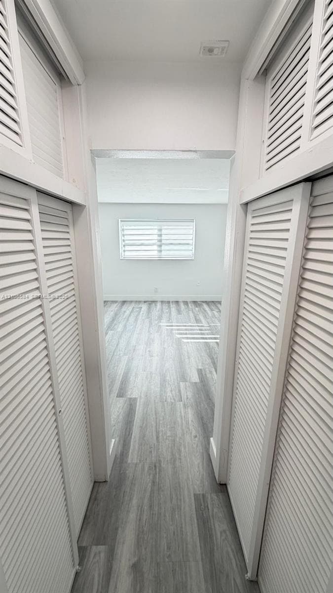 Hallway featuring louvered-style closet doors and wood-finish flooring