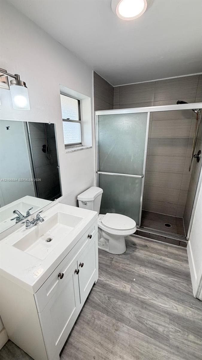 Bathroom featuring a white vanity with a rectangular sink, wood-finish flooring, a tiled walk-in shower with a glass enclosure, and modern brushed-metal fixtures
