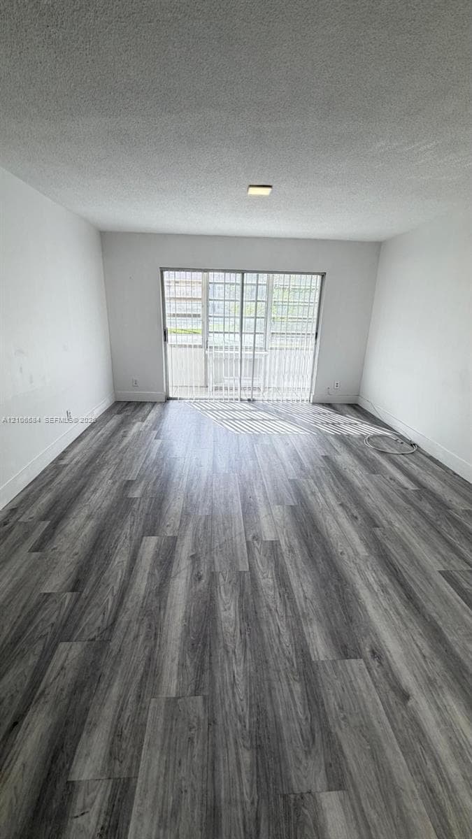 Room featuring wood-finish flooring, textured ceiling, and sliding glass door with vertical blinds