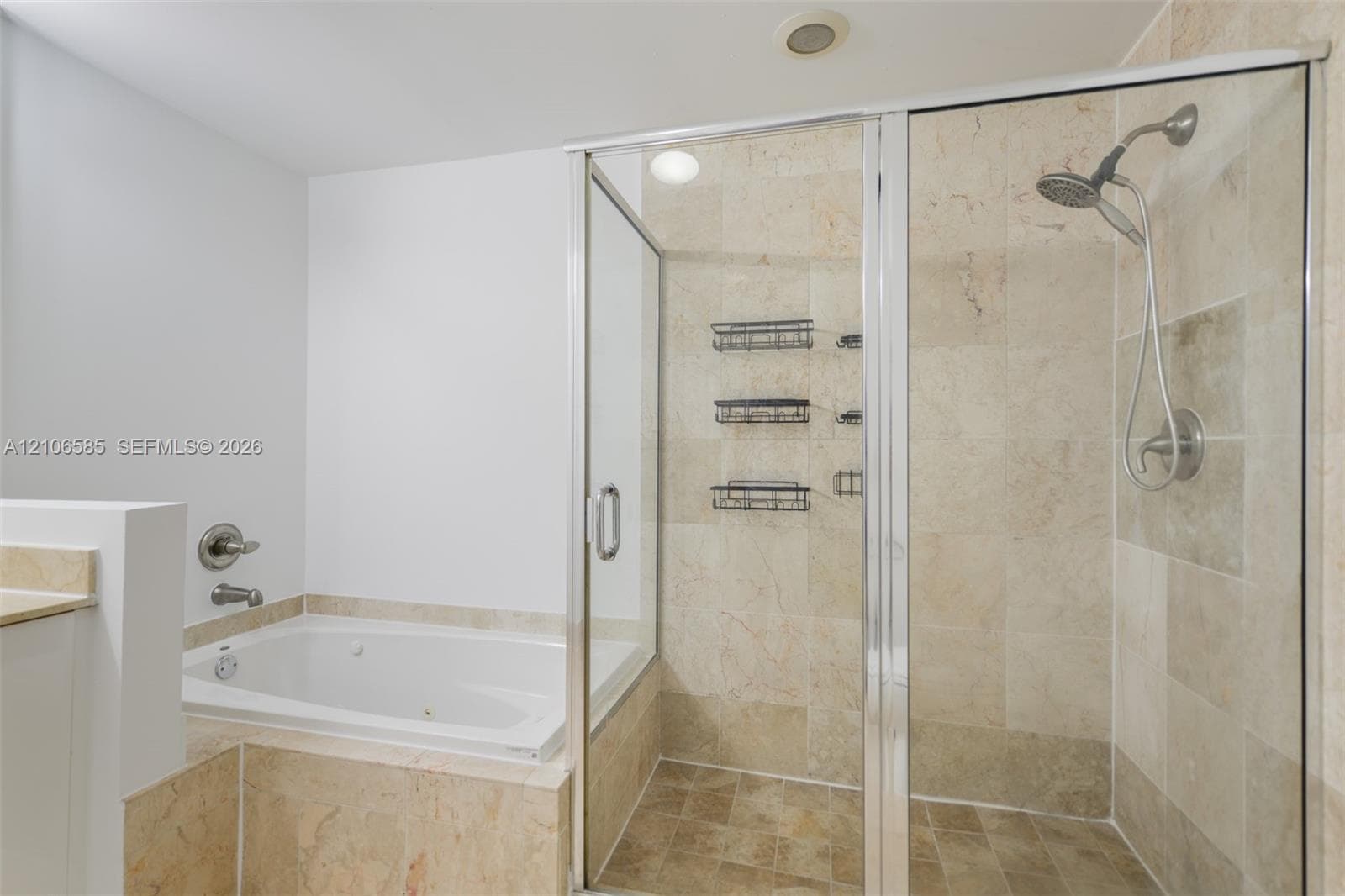 Jetted soaking tub with tile surround and separate glass-enclosed shower featuring stone-finish wall tiles and a handheld shower fixture