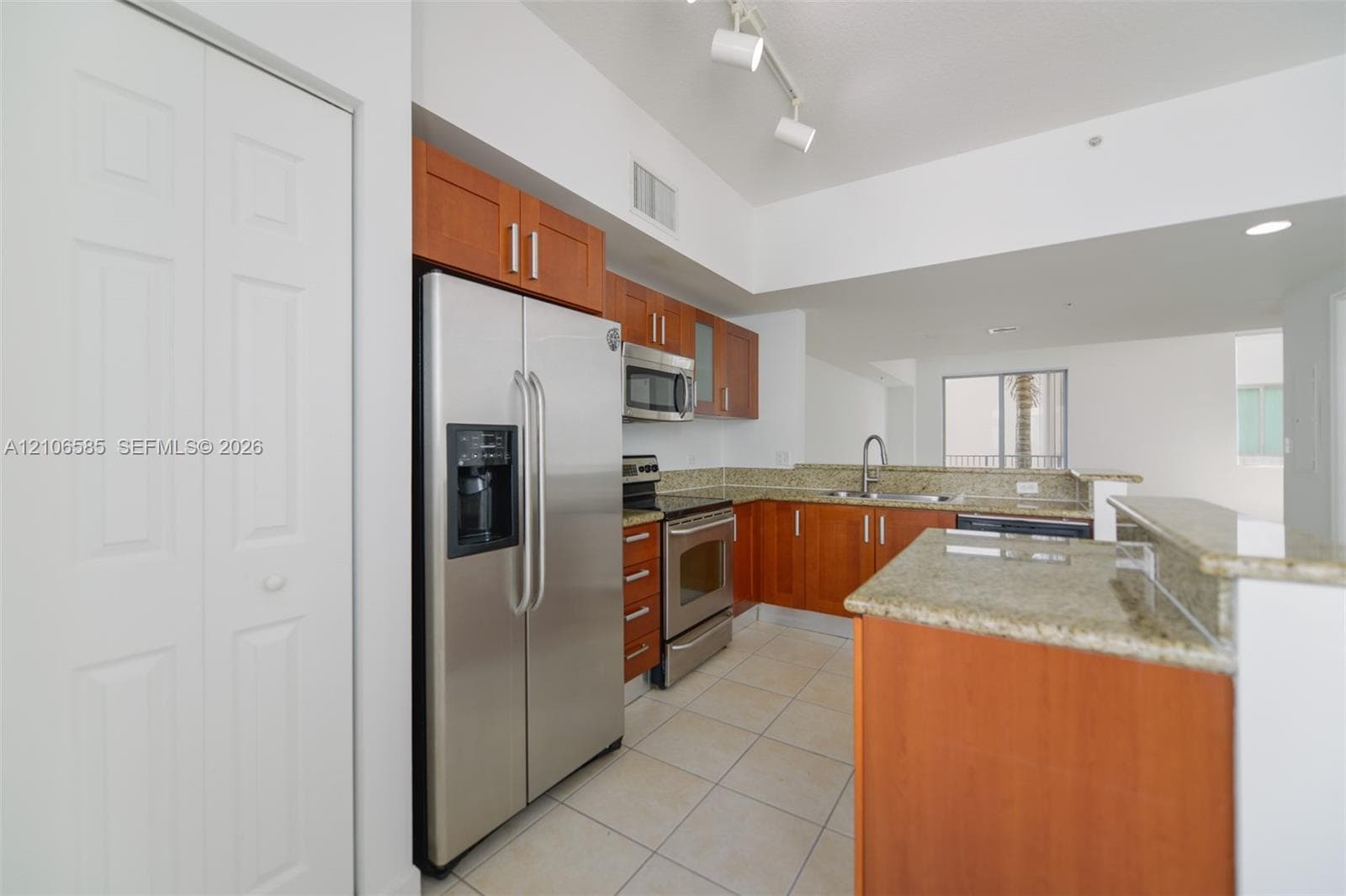 Kitchen featuring warm-tone wood cabinetry, stone countertops, stainless steel appliances, tile flooring, and track lighting