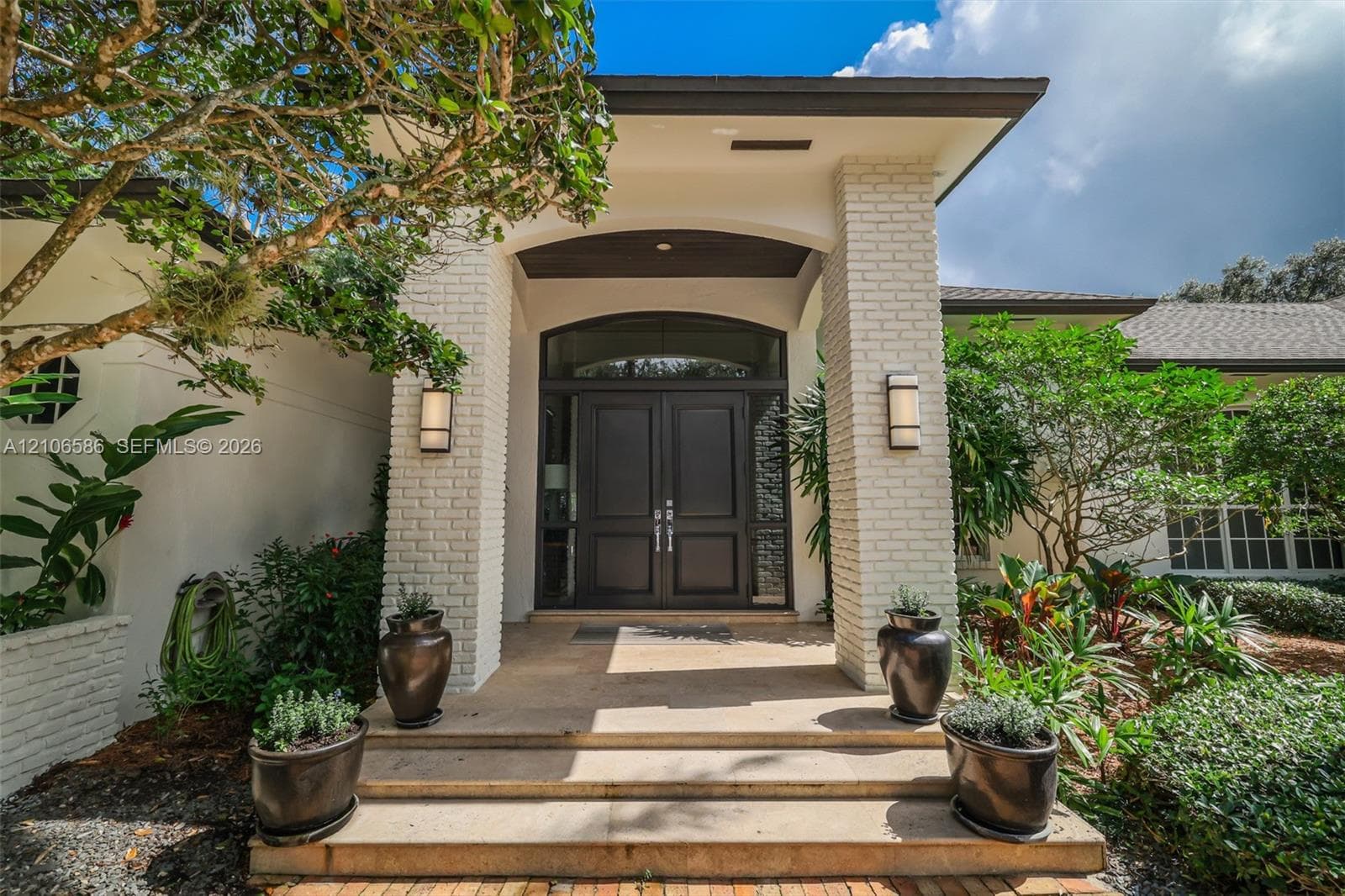 Covered entryway featuring light-colored brick columns, double front doors with arched transom windows, and stone steps