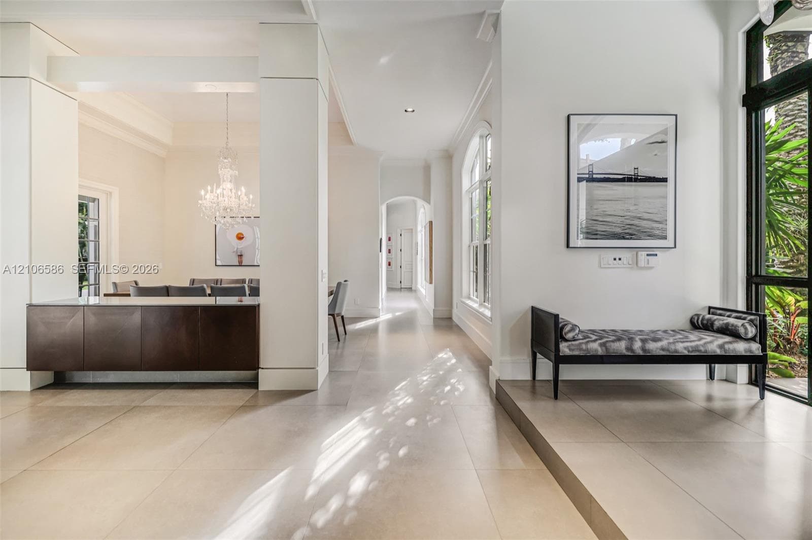 Interior space featuring large-format tile flooring, a dark-finish built-in console with a light-tone countertop, a crystal chandelier, arched architectural accents, and floor-to-ceiling windows