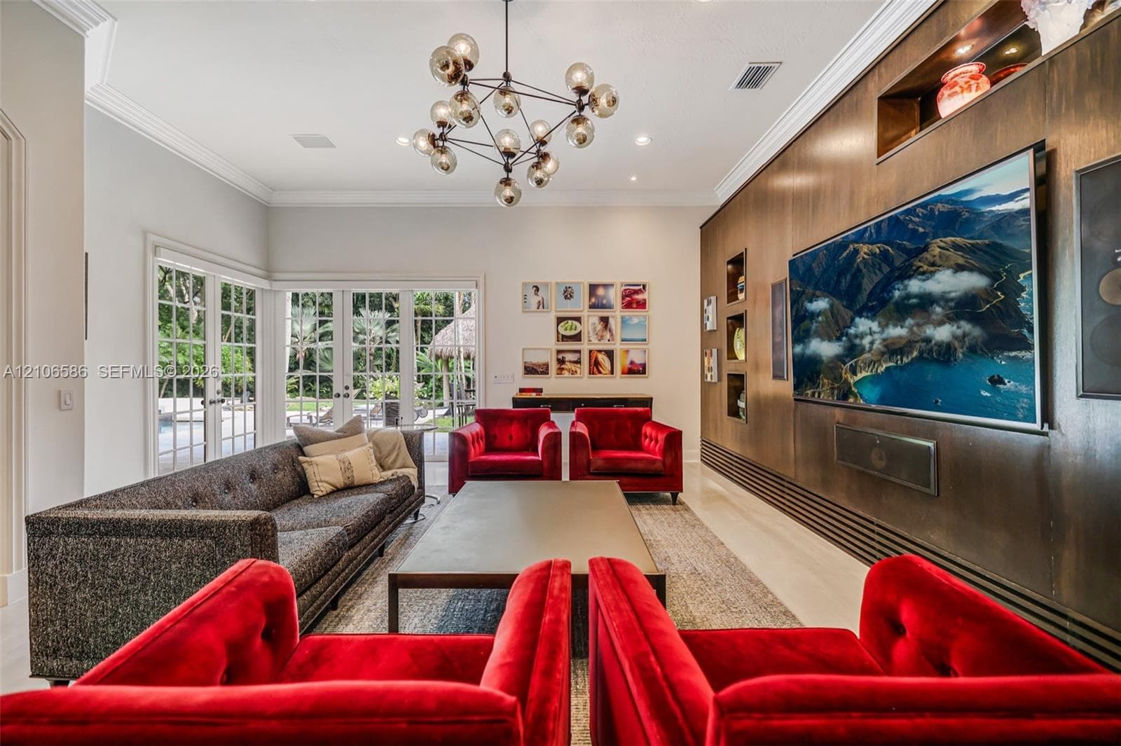 Living area featuring custom wood wall paneling with integrated shelving, multi-globe chandelier, recessed lighting, and full-height glass paneled doors