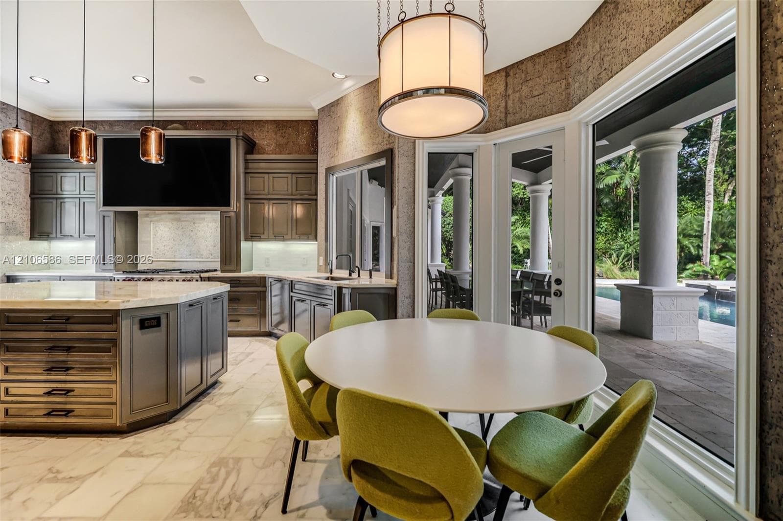 Kitchen featuring custom cabinetry, an oversized central island with stone countertop, large-format tile flooring, textured wall finishes, and expansive glass doors opening to a columned patio