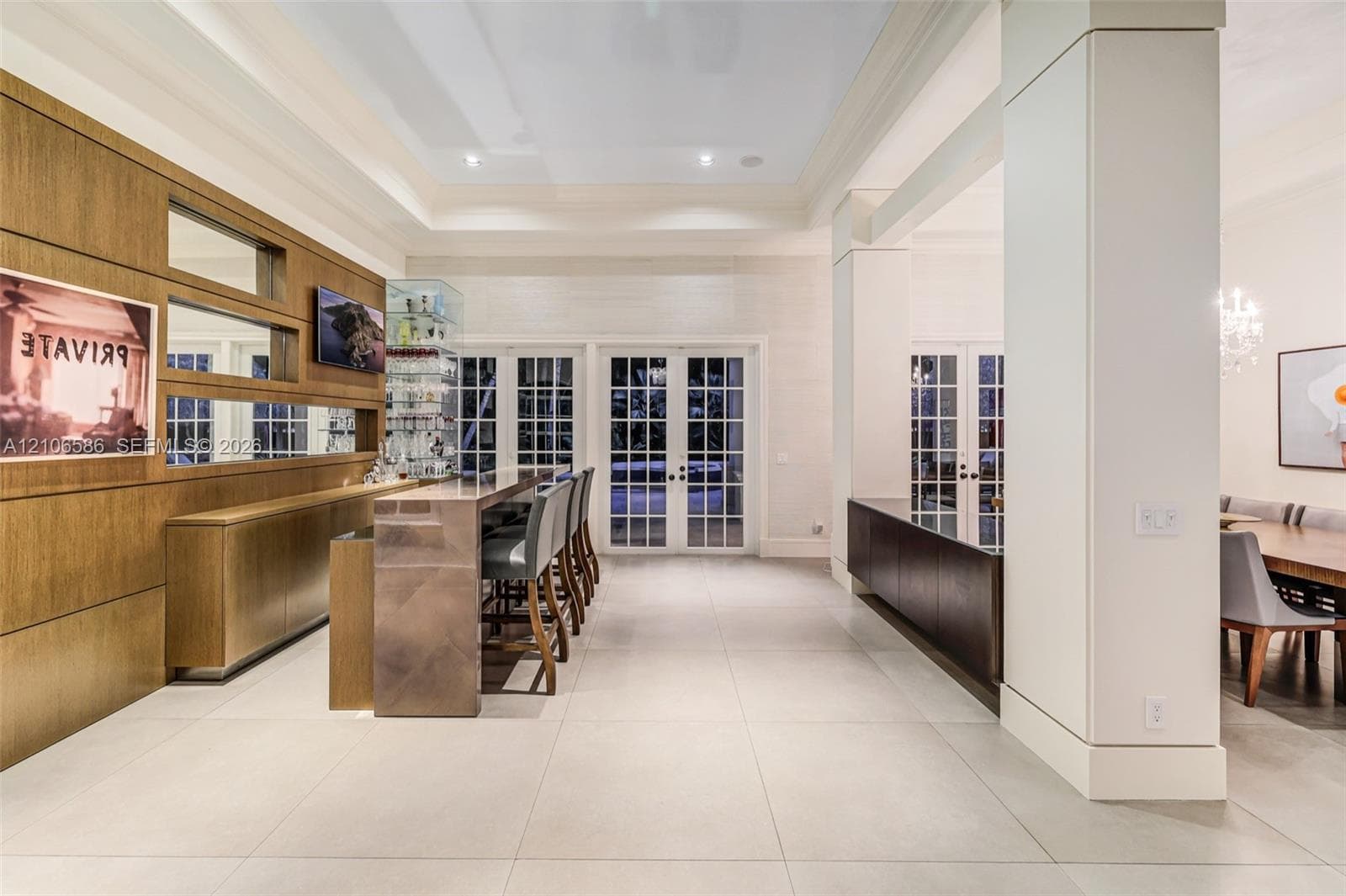 Custom bar w/ wood-paneled wall, lighted niches, glass display cabinet & bar seating, French doors to the terrace & formal dining beyond