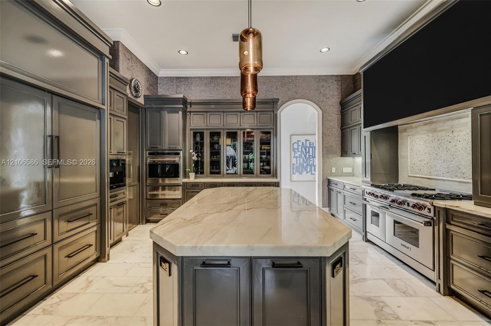 Custom cabinetry with integrated appliances, expansive central island with stone-finish countertop, professional-grade range, built-in display cabinetry, and polished stone-finish flooring