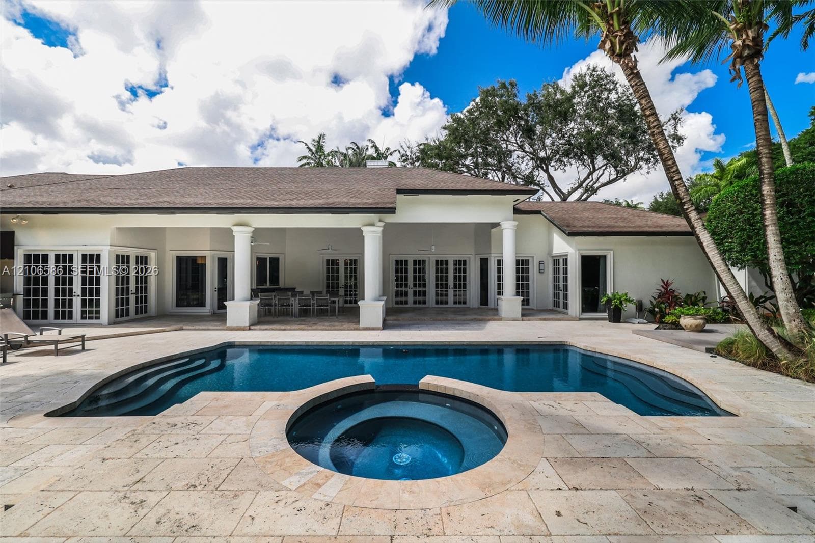 Covered patio with architectural columns, stone paver decking, and in-ground swimming pool featuring an integrated circular spa