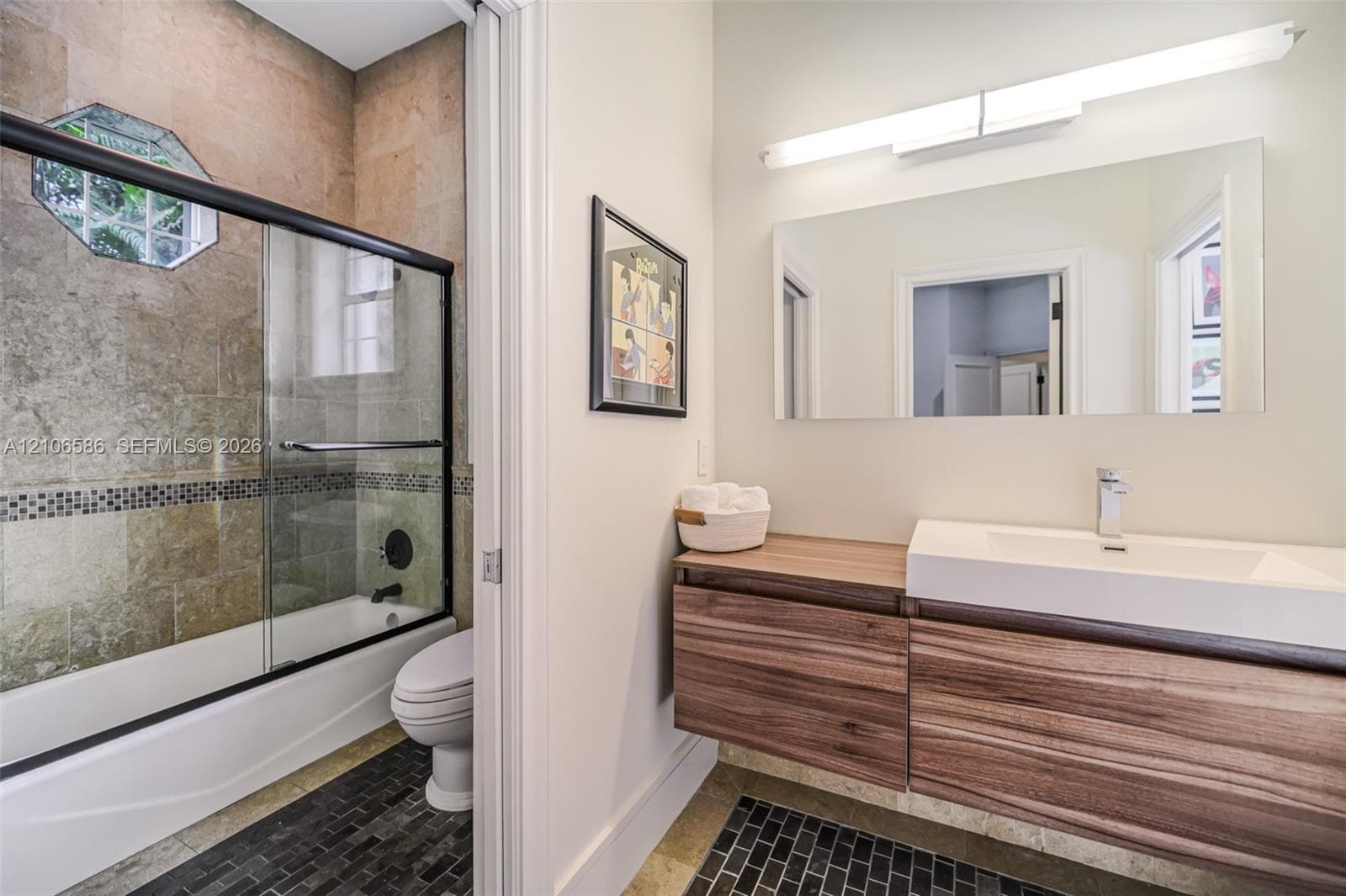 Floating wood-finish vanity with a rectangular integrated sink, wall-mounted rectangular mirror, shower enclosure featuring a glass sliding door, and stone-tiled shower surround