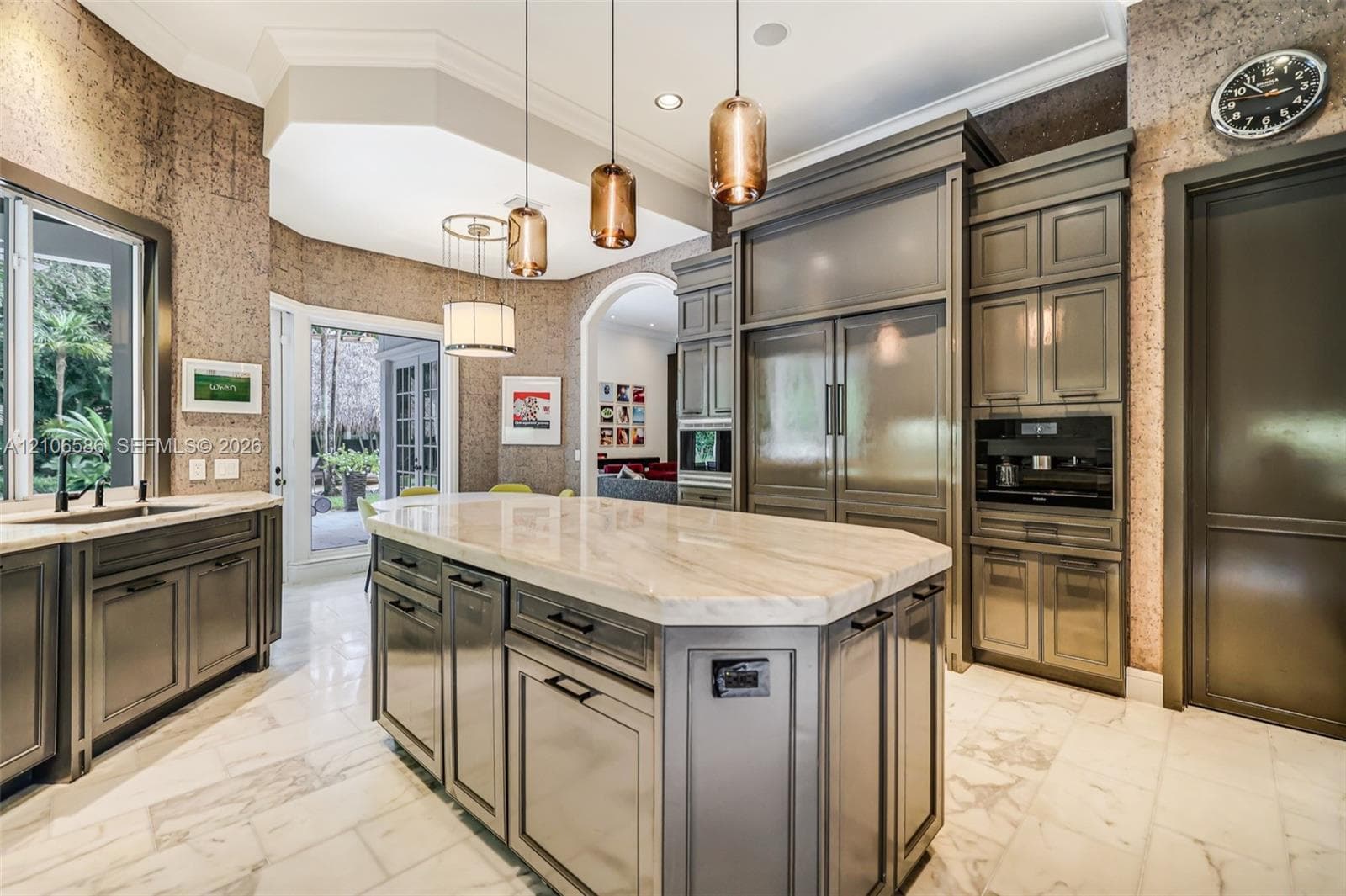Custom cabinetry with panel-ready integrated appliances, expansive stone-topped central island, polished stone flooring, and multi-pendant lighting