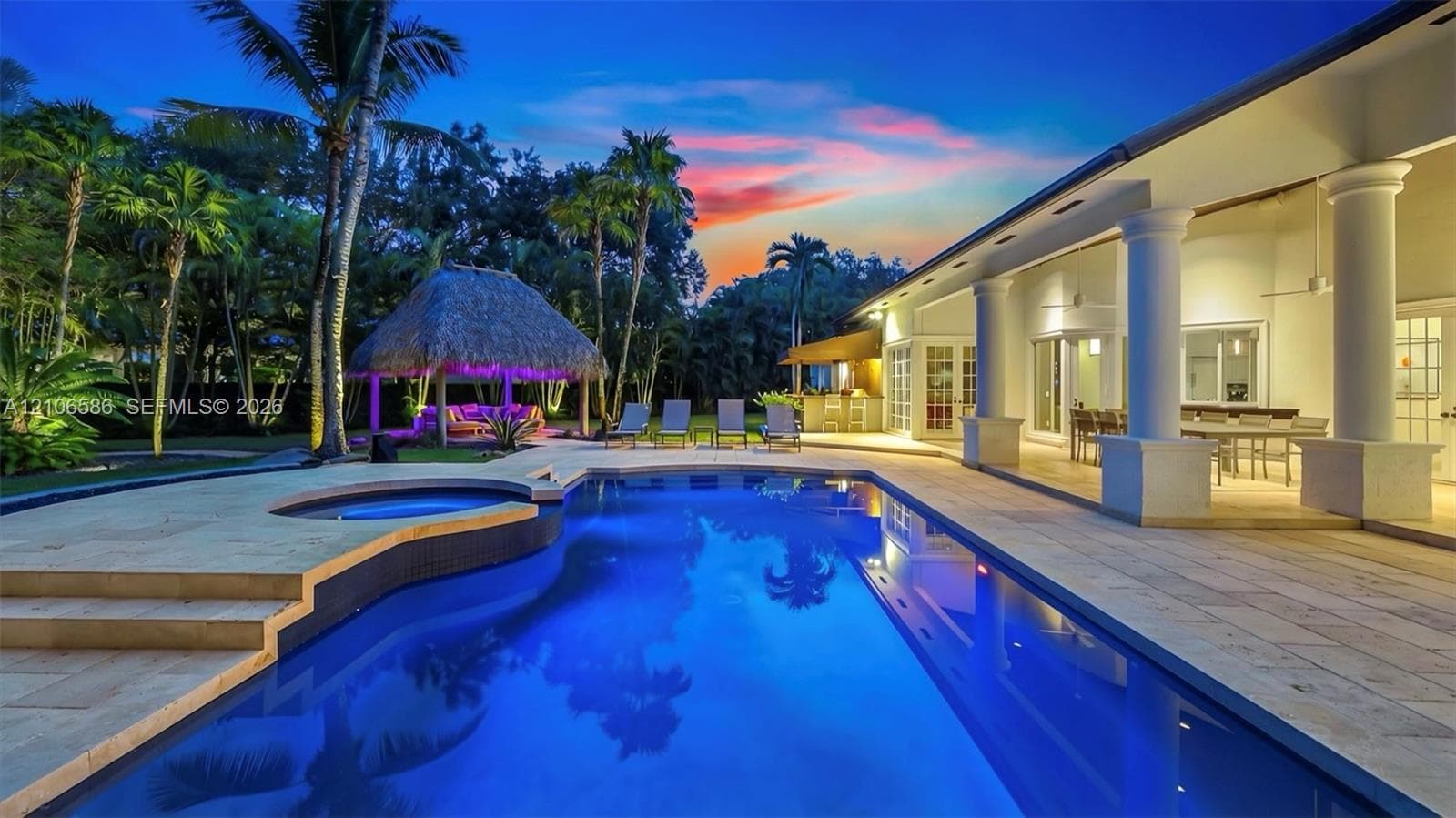 Custom swimming pool with integrated spa, expansive stone patio, covered lanai featuring structural columns, and a thatched-roof cabana