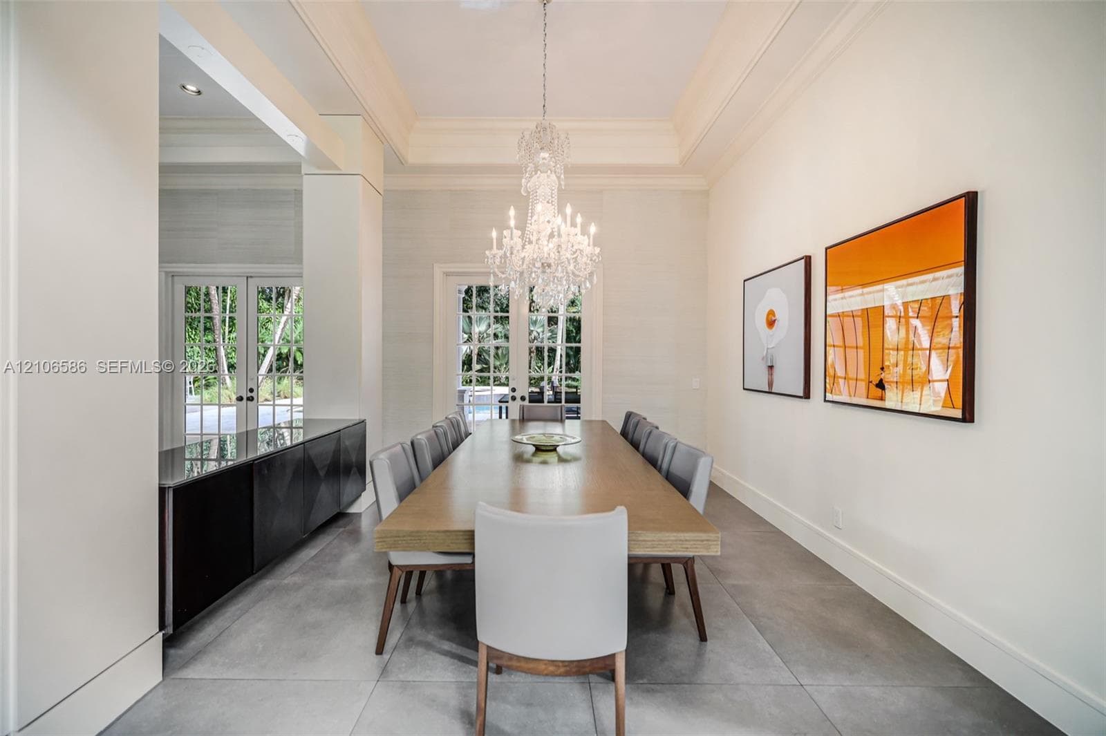 Formal room featuring a tray ceiling, crystal chandelier, large-format tile flooring, built-in cabinetry with a stone countertop, and multi-pane glass doors