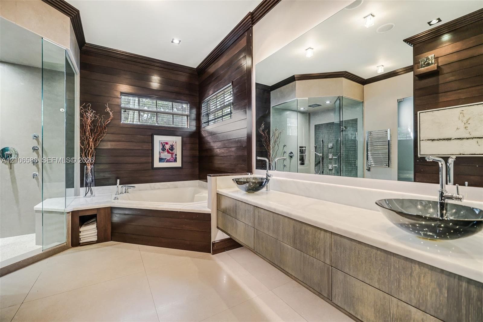 Dual vessel sinks with chrome faucets, stone-topped floating vanity, glass-enclosed shower, soaking tub, and horizontal wood-paneled walls