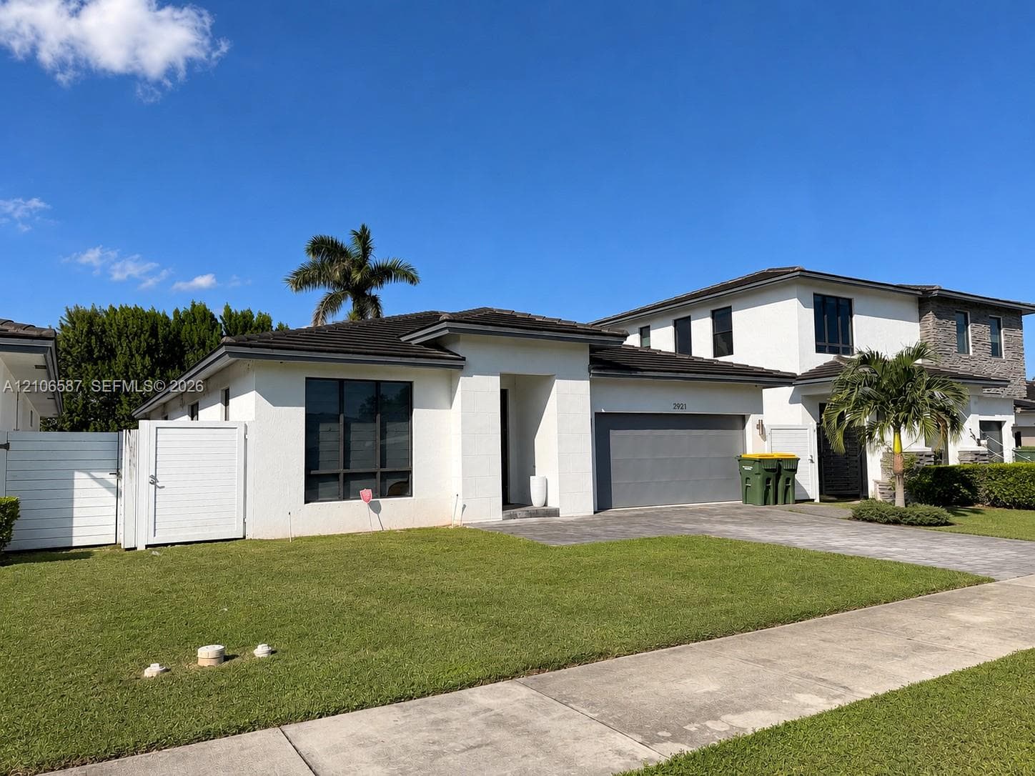 Single-story exterior featuring white stucco siding, a multi-car garage, a paver driveway, and a white privacy fence