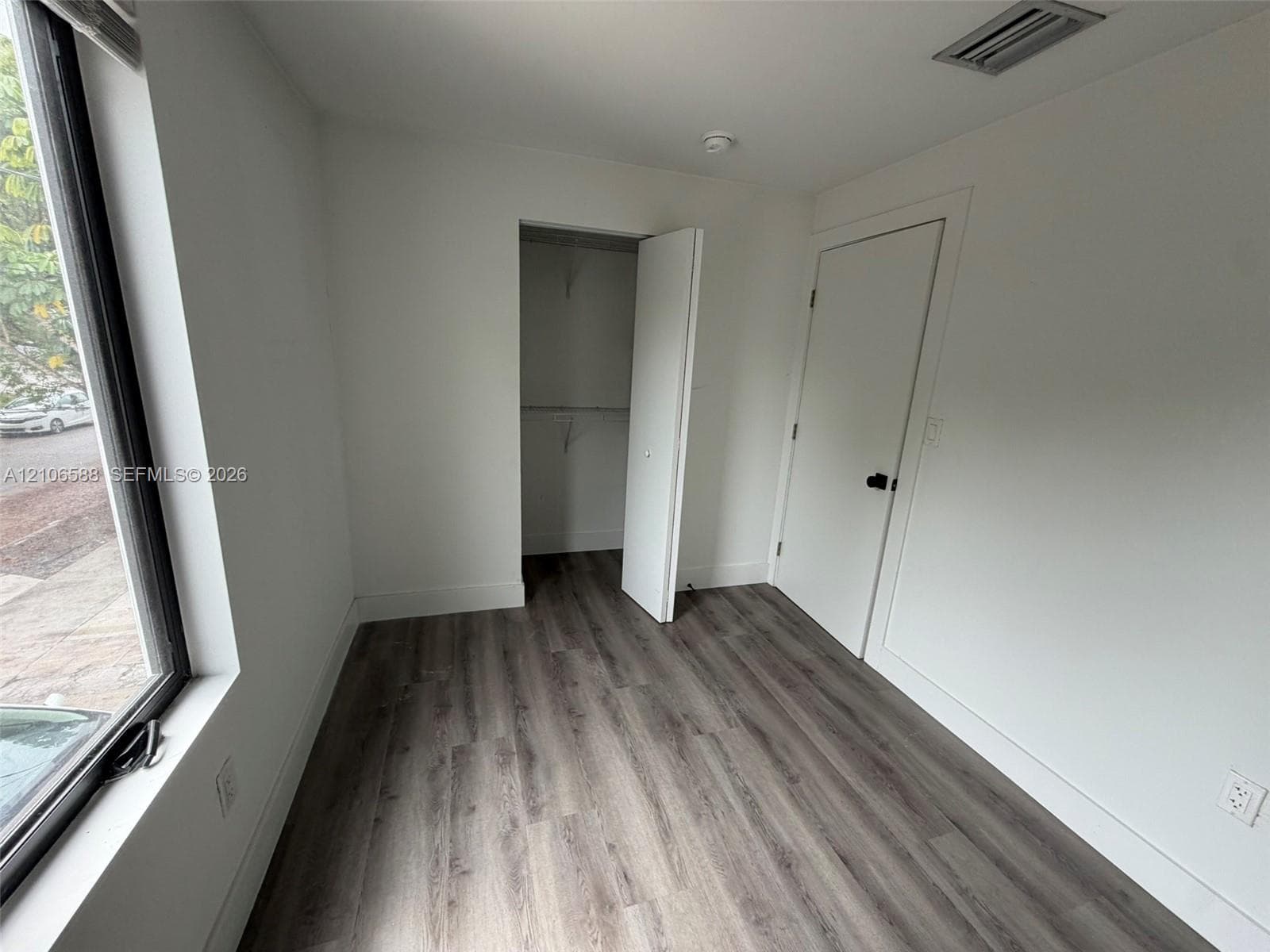 Neutral-toned interior featuring wood-finish flooring, a full-height window, and a built-in reach-in closet with integrated shelving