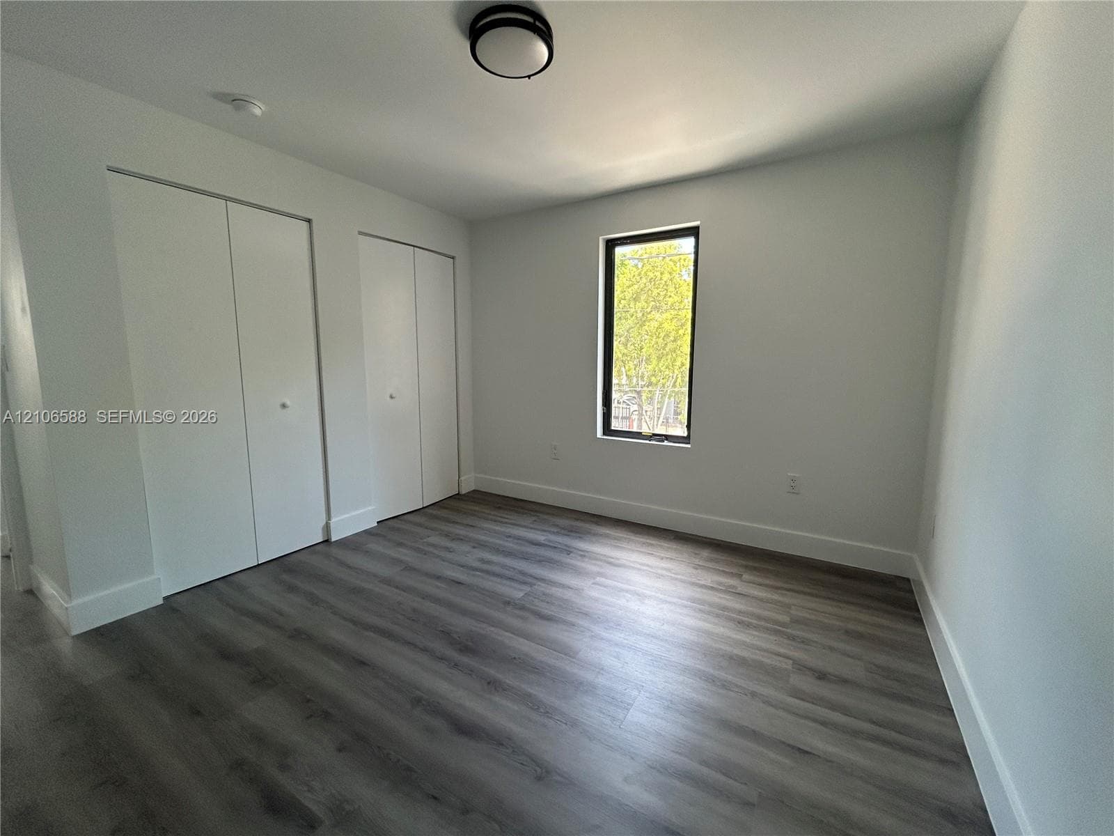 Wood-finish flooring, dual built-in closets with white panel doors, and neutral wall tones complemented by a ceiling-mounted light fixture