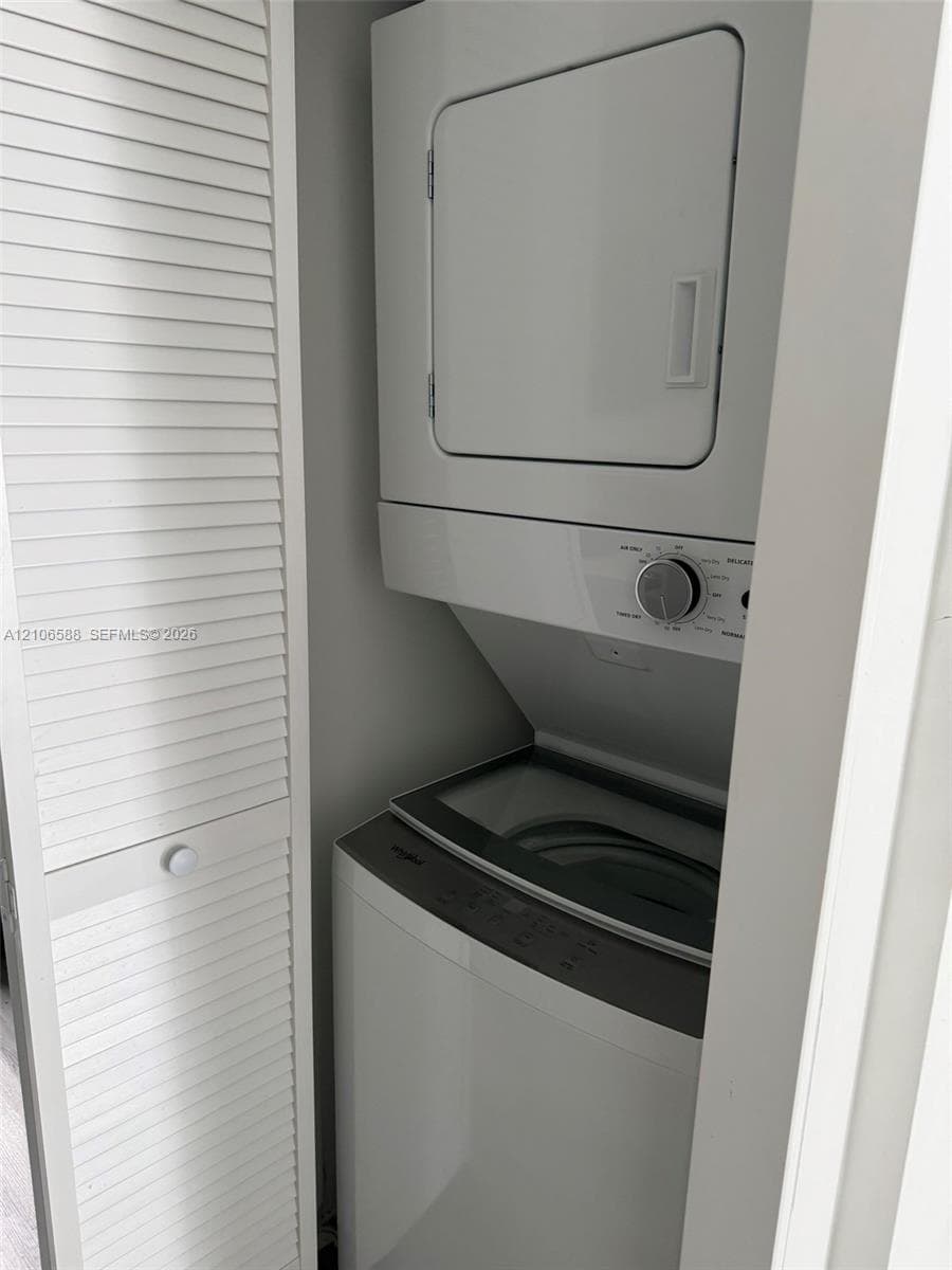 Stacked laundry unit housed within a closet featuring white louvered doors