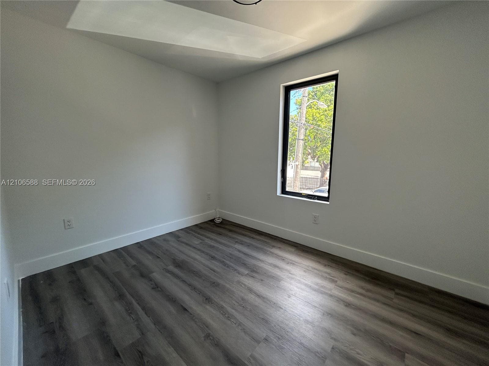 Neutral interior space featuring wood-finish flooring, smooth-finish walls, and a tall rectangular window with a black frame