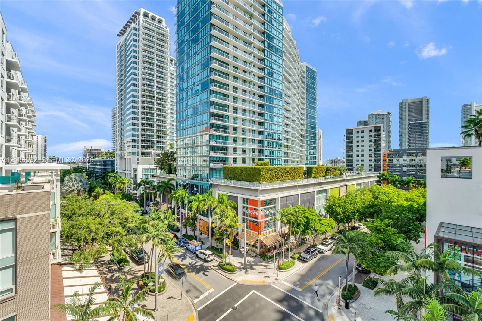 High-rise exterior featuring floor-to-ceiling glass paneling, multi-level structural design, manicured rooftop greenery, and ground-level storefronts with metal framing