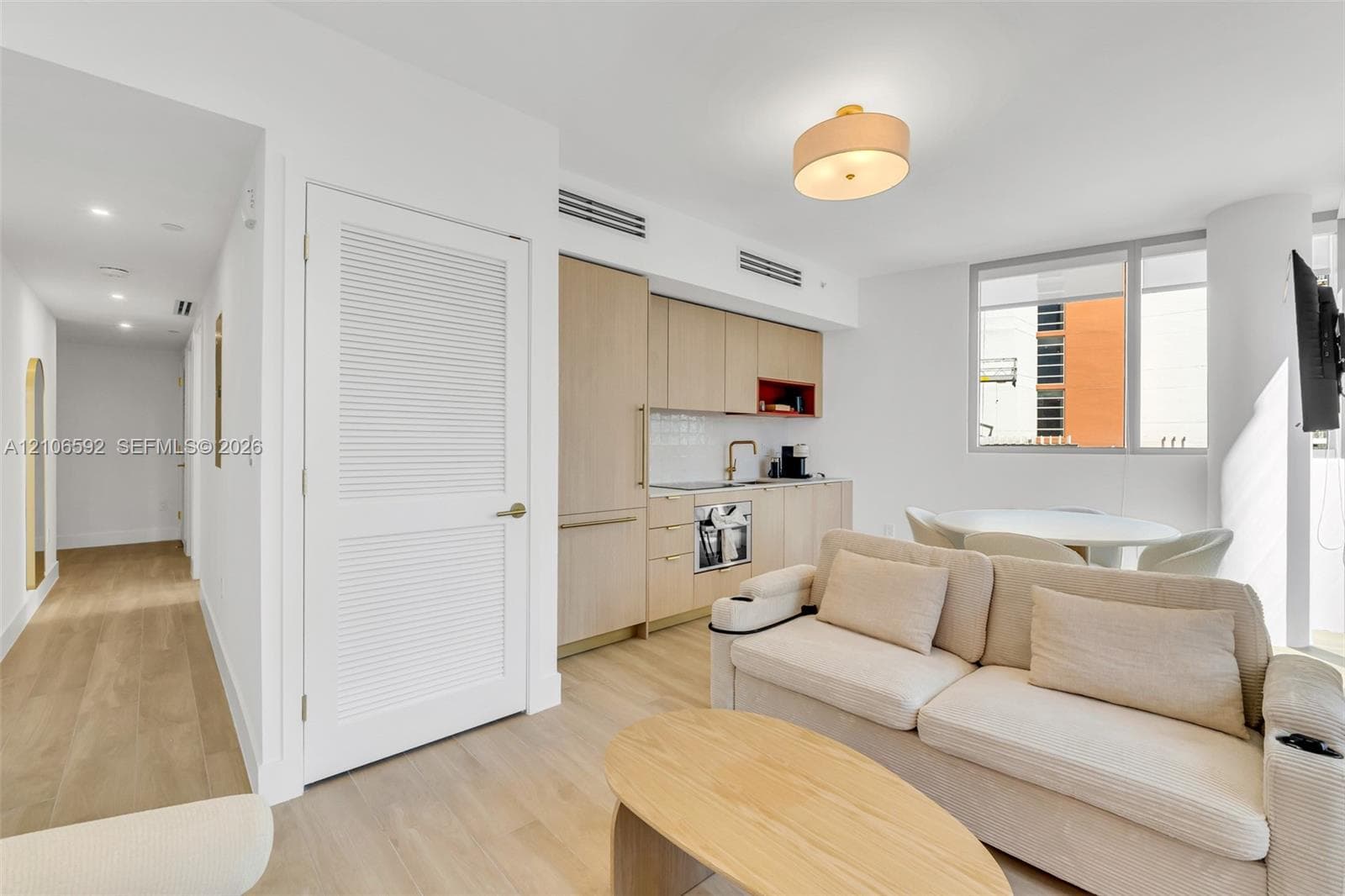 Light-toned cabinetry, wood-finish flooring, built-in panel-ready appliances, louvered closet door, and drum ceiling lighting