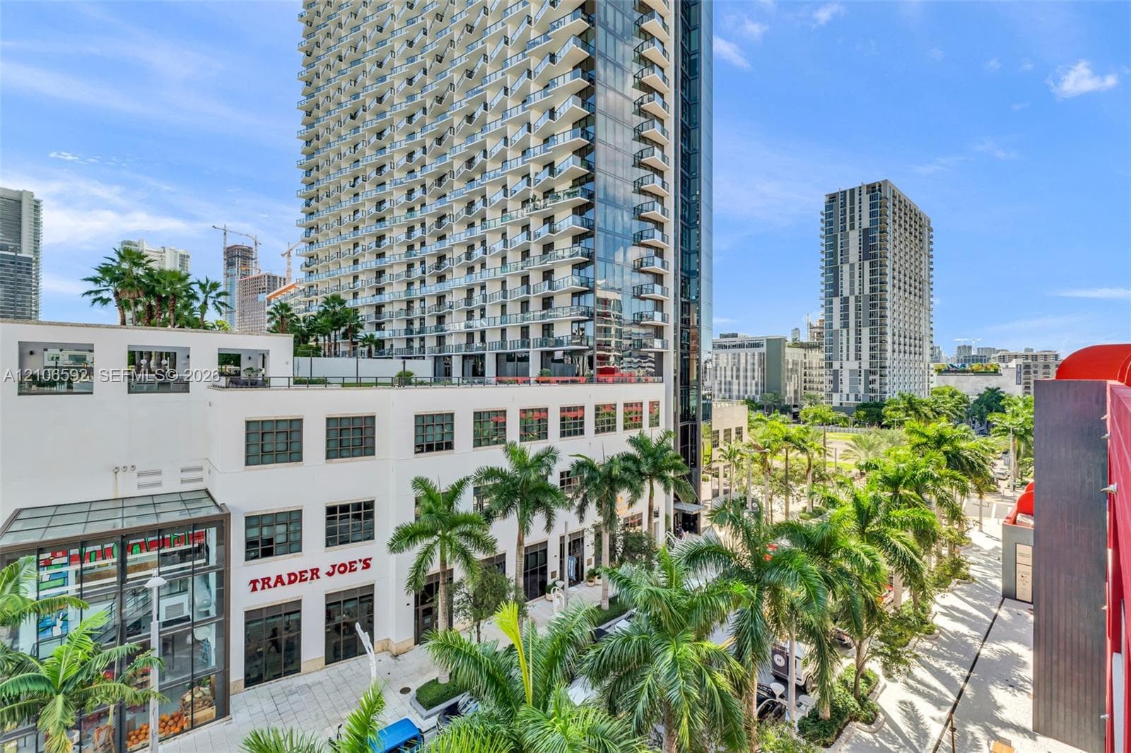 High-rise architecture featuring extensive glass curtain walls, private balconies, a multi-story podium structure, and landscaped grounds with mature palm trees