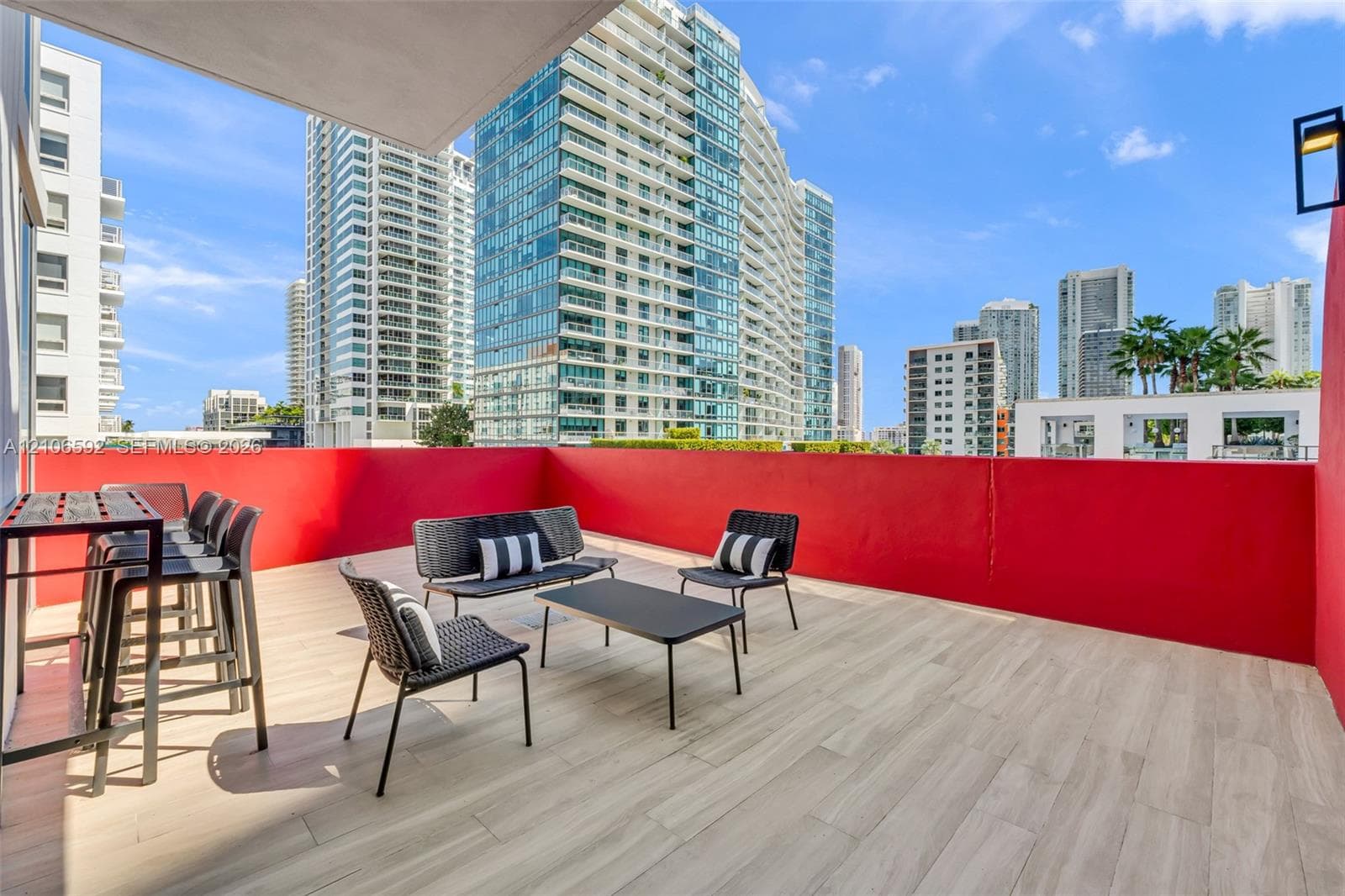 Open-air balcony featuring wood-finish tile flooring, solid red privacy walls, and a wall-mounted light fixture