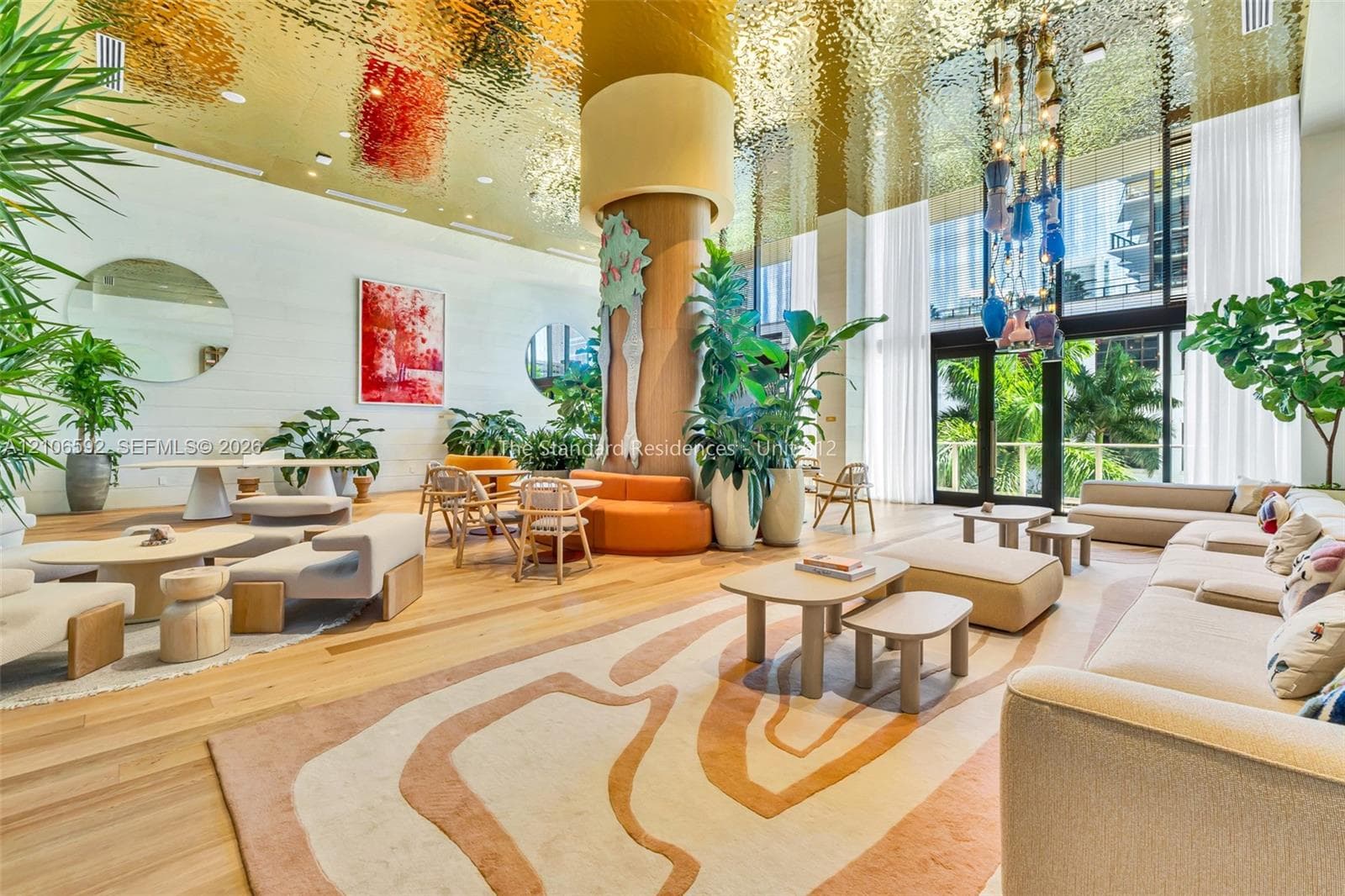 Reflective metallic ceiling, floor-to-ceiling windows, wood-finish flooring, central structural column, and custom decorative lighting fixture