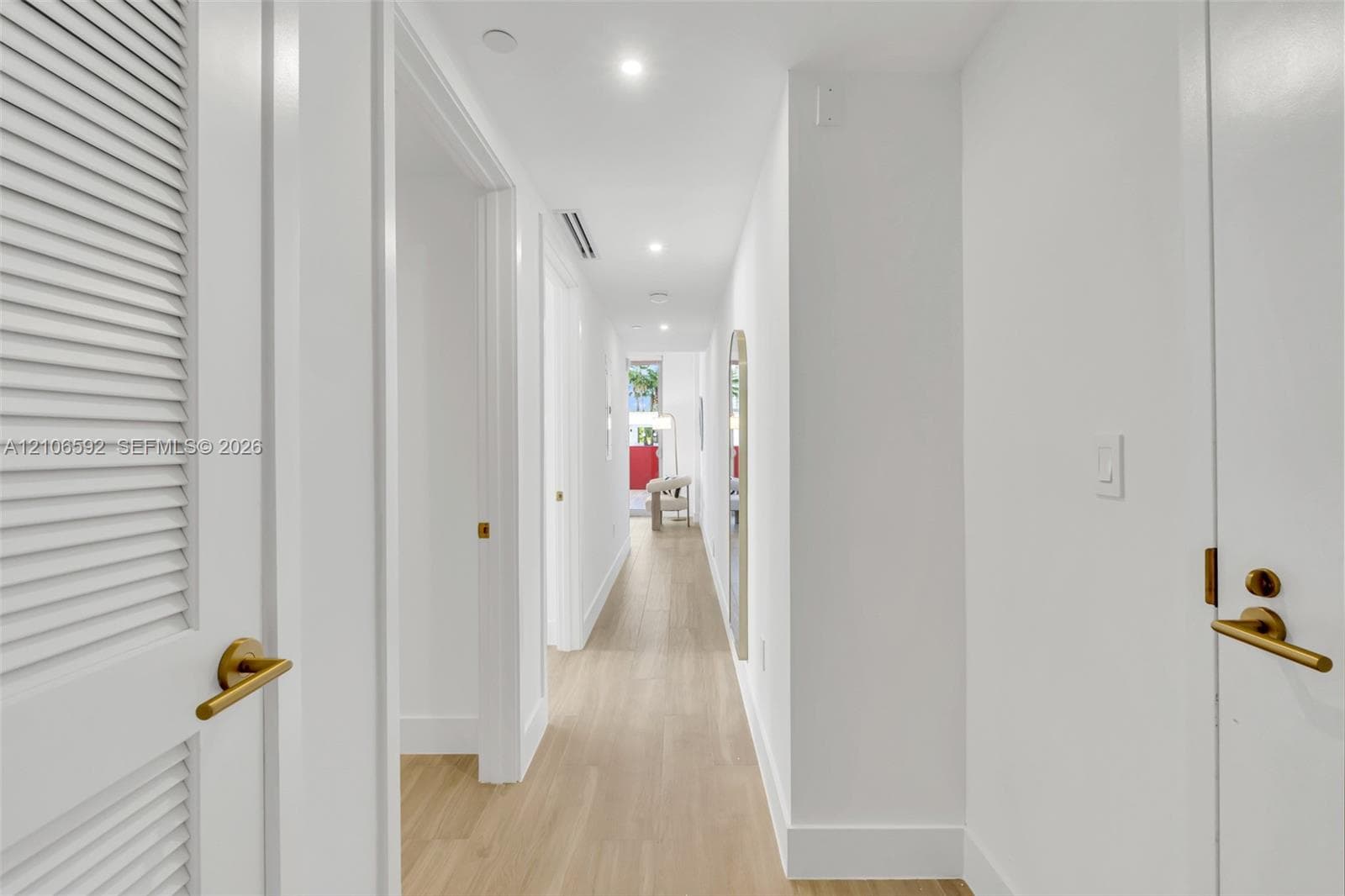 Hallway featuring wood-finish flooring, recessed lighting, and doors with gold-tone hardware, including a louvered closet door