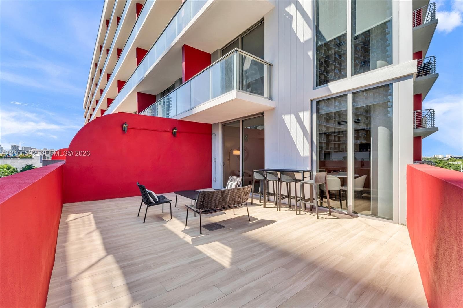 Expansive private terrace featuring wood-finish flooring, full-height glass sliding doors, and contrasting solid masonry walls