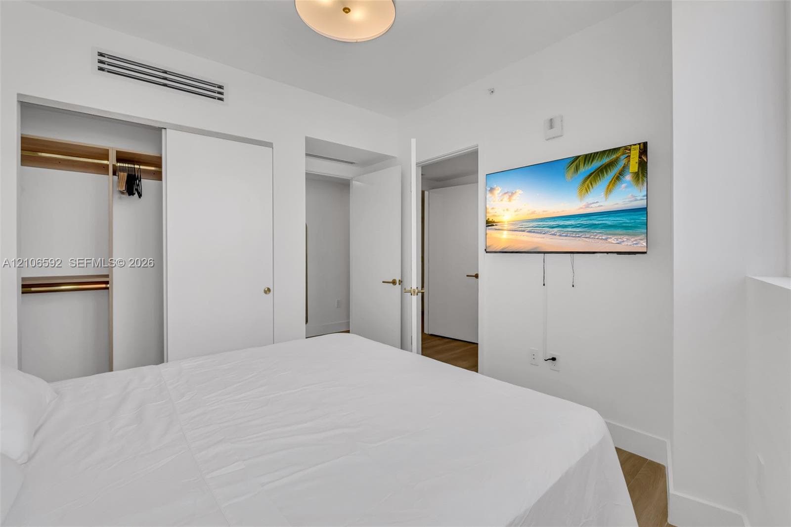 Room featuring wood-finish flooring, ceiling-mounted light fixture, sliding door closet with built-in shelving, and integrated climate control unit