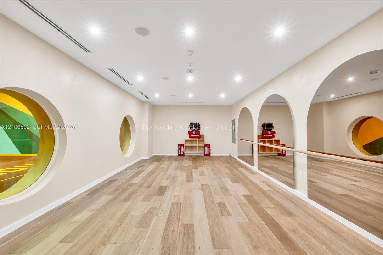 Interior space featuring wood-finish flooring, recessed lighting, arched wall mirrors, a mounted ballet barre, and circular window accents