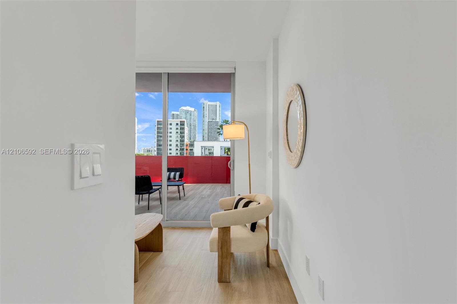 Sliding glass door leading to a balcony with wood-finish flooring and a red metal railing, featuring wood-finish flooring throughout the interior